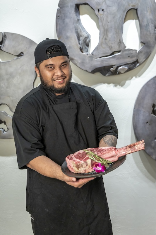 Chef presenting a raw American Wagyu tomahawk steak at Empire Steak House Hawaii