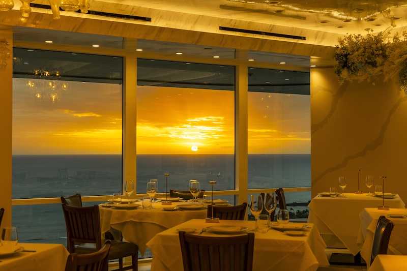 Bright contemporary dining room with floor-to-ceiling windows overlooking the Pacific at sunset, Empire Steak House Hawaii