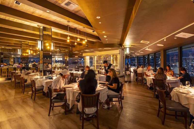 Guests dining at Empire Steak House Hawaii in the evening beside the wine wall