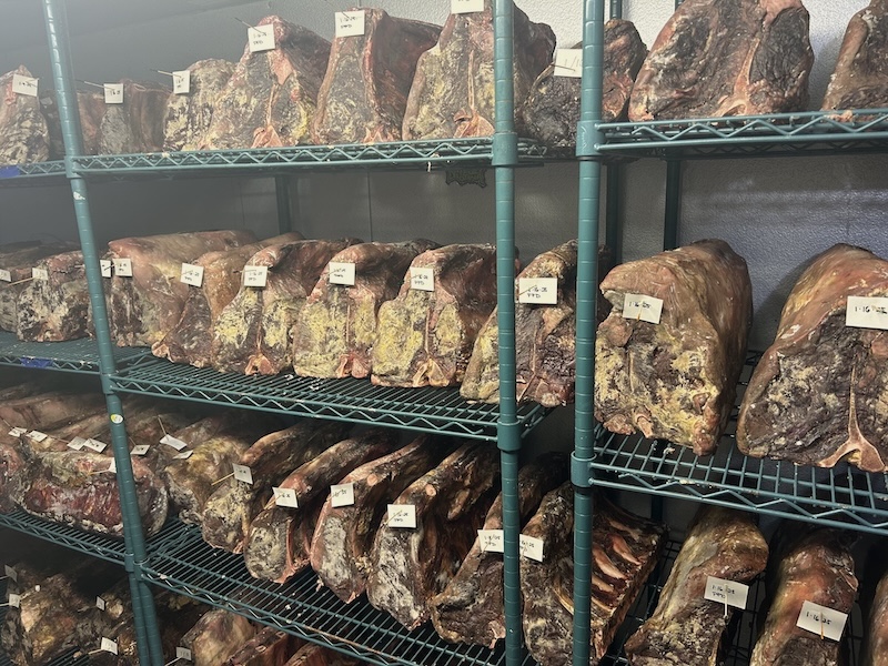 Beef dry-aging on racks with dated tags in the in-house aging room at Empire Steak House Hawaii