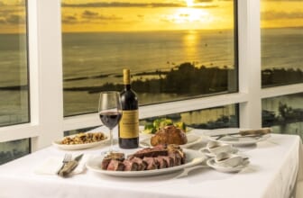Sliced USDA Prime steak and red wine set against a sunset ocean view at Empire Steak House Hawaii in Waikiki