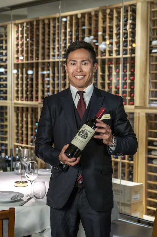 Staff member presenting a bottle in front of the wine wall at Empire Steak House Hawaii, which stocks more than 400 labels
