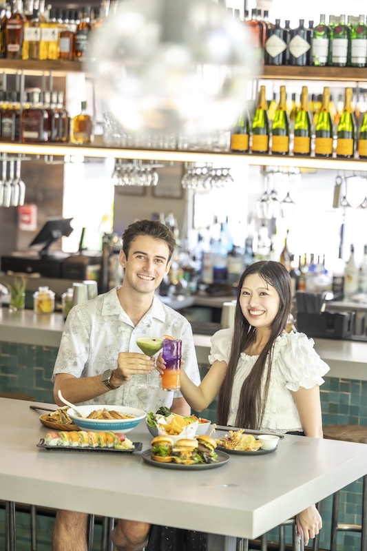 Two guests toasting cocktails at the bar counter during happy hour at Kamukura Surf + Dine in Waikiki
